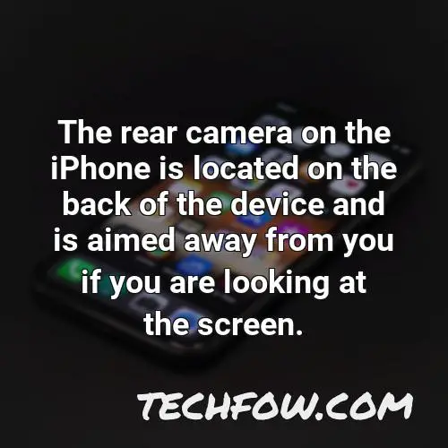 the rear camera on the iphone is located on the back of the device and is aimed away from you if you are looking at the screen